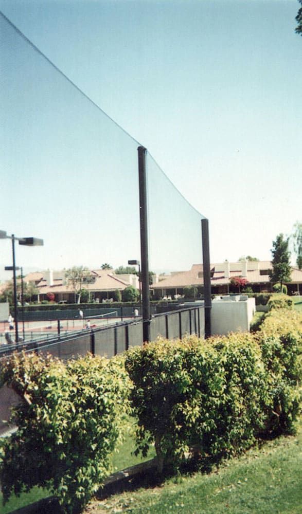 Baseball stadium with empty green and white bleachers, protective netting fence, and a well-maintained grass field under a clear blue sky.