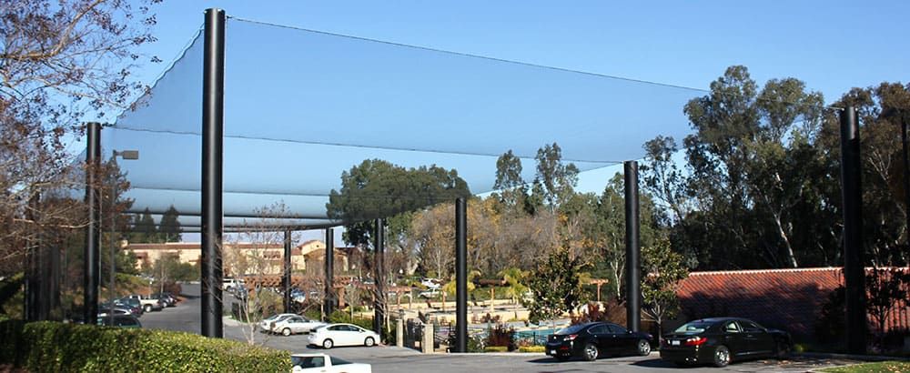 A parking lot covered by a golf protection struture netting system, surrounded by trees and bushes.