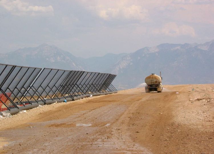 A water tanker truck drives along a dirt road next to a long row of Coastal Netting’s portable litter fences. There are mountains visible in the background.