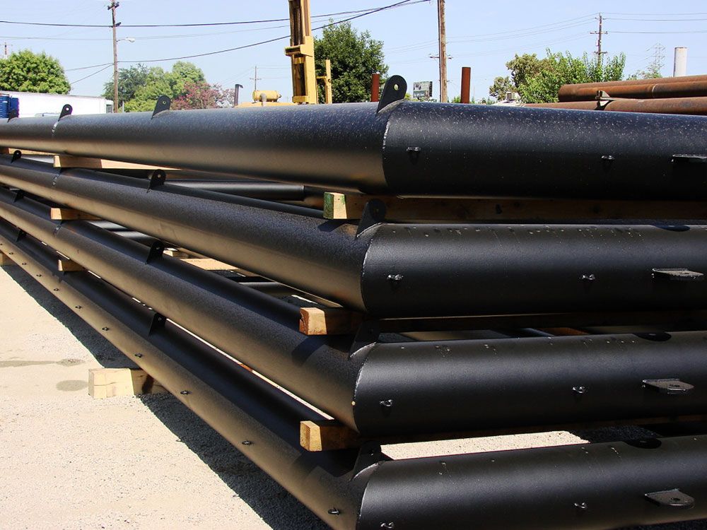 Coastal steel netting poles stacked with wooden spacers in an outdoor industrial storage area.