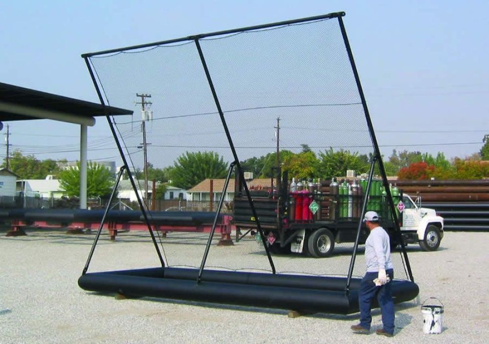 A worker stands next to a 16-foot tall portable litter fence outdoors. A truck with gas cylinders is parked in the background.