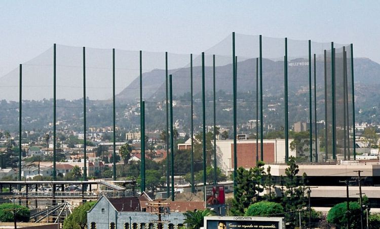 Wide view showing tall Coastal-built netting system with steel poles around a driving range. The Hollywood sign is visible on the hills in the background, overlooking a bustling urban area.