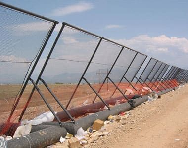 A row of Coastal Netting’s portable litter fences along a dirt road, with construction materials and litter debris collected at the base of the fences.
