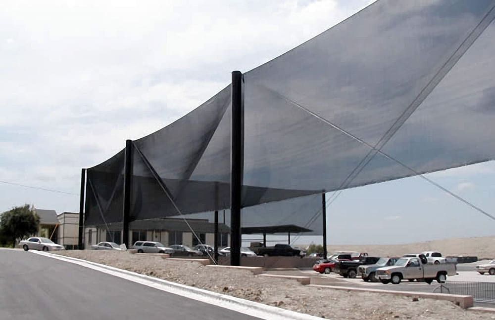 A large windscreen structure installed over a parking lot with several cars parked underneath.